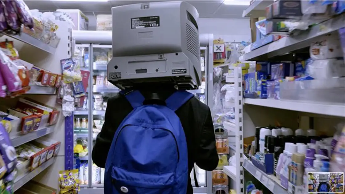 view of the back of boy walking down the aisle in a shop, with a rucksack on his back and a telly monitor on his head